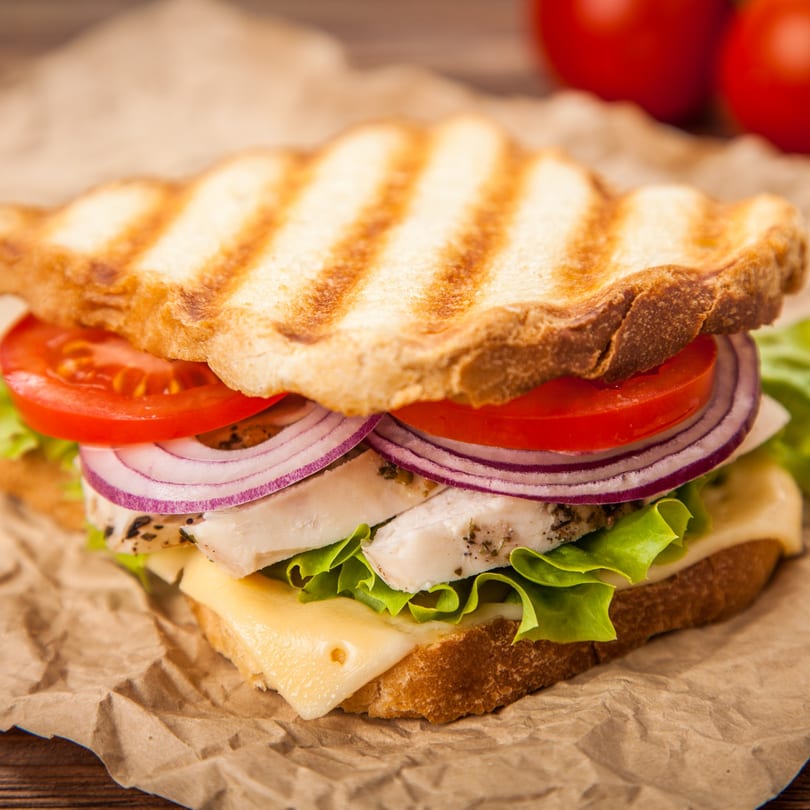Grilled chicken sandwich with lettuce, tomato, red onion, and cheese on toasted bread.