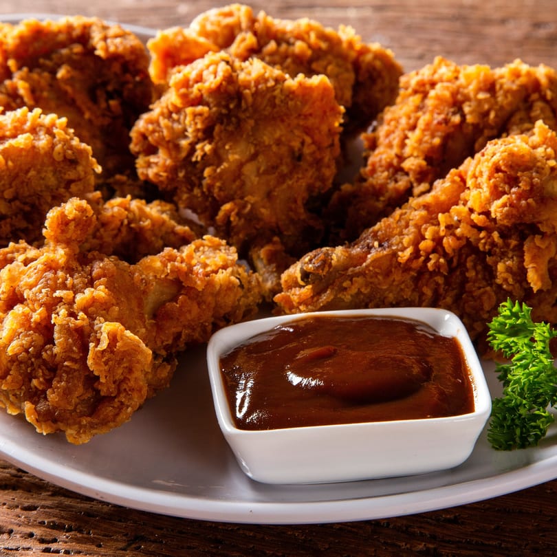 Crispy fried chicken pieces with a side of barbecue sauce and parsley on a white plate.
