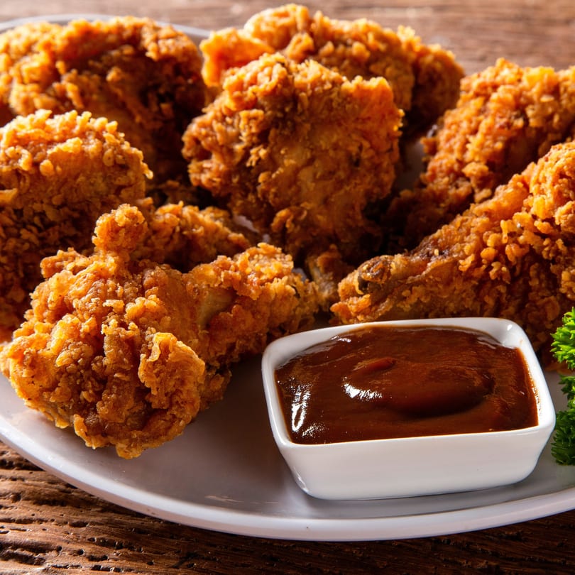Crispy fried chicken pieces on a white plate with a side of barbecue dipping sauce.