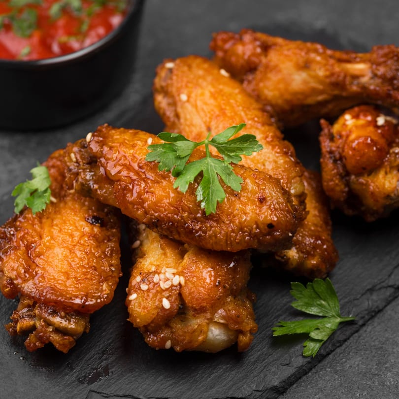 Big Daddy's Pizza & Wings' golden-brown chicken wings, garnished with parsley and sesame seeds, with dipping sauce.